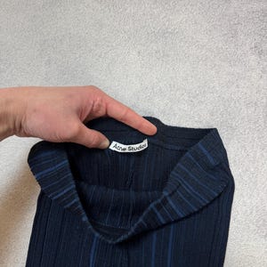 Puede incluir: Pantalones de punto acanalado azul marino oscuro con rayas verticales. Los pantalones tienen una cintura alta y una etiqueta que dice "Acne Studios". La tela parece ser un material suave y el&aacute;stico.