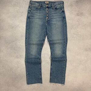 Può includere: Jeans di denim blu chiaro con chiusura a bottoni. Questi jeans a vita alta hanno una gamba dritta e un orlo grezzo sfilacciato. Il denim ha un aspetto sbiadito e una leggera usura.