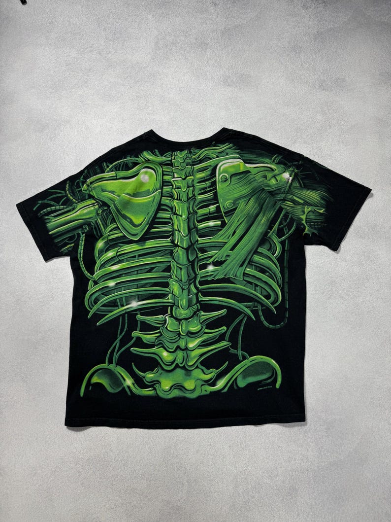Puede incluir: Camiseta negra con un dise&ntilde;o de esqueleto verde vibrante. El gr&aacute;fico incluye una detallada caja tor&aacute;cica, columna vertebral y om&oacute;platos, creando un efecto visual impactante. La camiseta es de cuello redondo y manga corta.