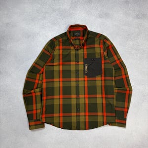 May include: A green and orange checked shirt with a black pocket. The long-sleeved shirt has a button-down front and a collared neckline. The word "TIDURUE" is printed vertically on the pocket.