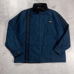 Puede incluir: Chaqueta azul marino con cuello negro y rayas negras en la parte delantera. La chaqueta tiene cierre de cremallera, un pequeño bolsillo y la palabra "gouge" bordada en el pecho. Mangas largas y cierre de botón en los puños.