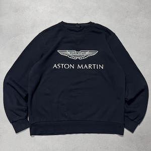 Puede incluir: Sudadera azul marino con el logotipo blanco de Aston Martin. El logotipo es un diseño de ala estilizada sobre las palabras "ASTON MARTIN". La sudadera tiene cuello redondo y mangas largas.