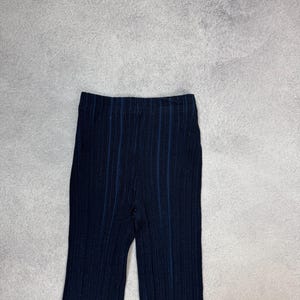 Puede incluir: Pantalones de punto acanalado azul marino oscuro con rayas azules verticales. Los pantalones tienen una cintura alta y una pernera ancha. La tela parece ser un material suave y el&aacute;stico. Los pantalones se muestran sobre un fondo gris neutro.