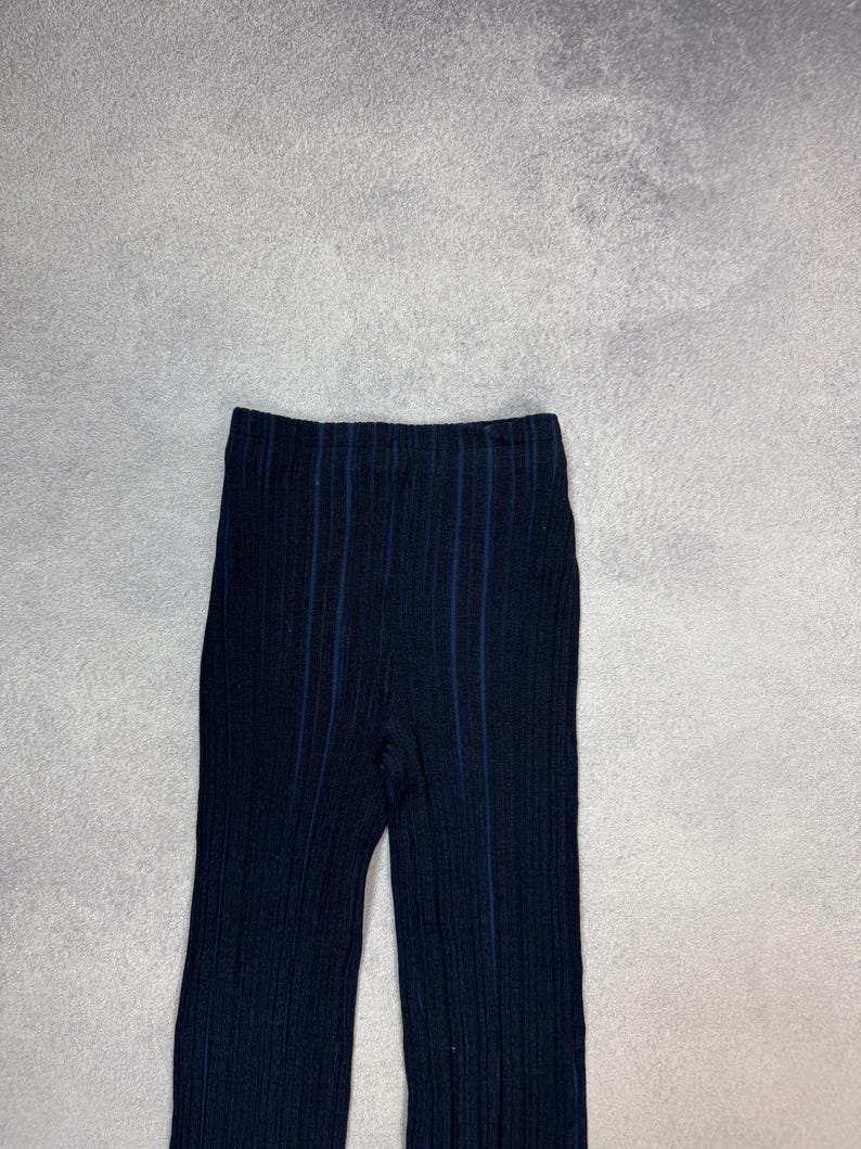Puede incluir: Pantalones de punto acanalado azul marino oscuro con rayas azules verticales. Los pantalones tienen una cintura alta y una pernera ancha. La tela parece ser un material suave y el&aacute;stico. Los pantalones se muestran sobre un fondo gris neutro.