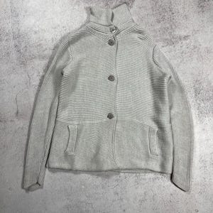 May include: A light gray, ribbed knit cardigan with a high, buttoned collar. The sweater has three buttons down the front and two small pockets. The sleeves are long, and the overall style is classic and versatile.
