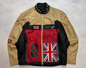 Op de afbeelding: Tan en zwarte racejas met rode en zwarte accenten. Voorzien van een Union Jack-patch, het nummer 9 en sponsorlogo's. De jas heeft een ritssluiting aan de voorkant en een opstaande kraag.