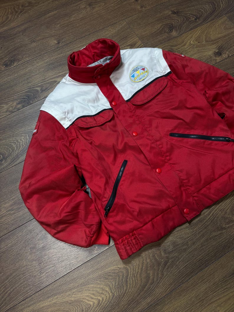 May include: Red and white vintage jacket with a stand-up collar, two front pockets, and a zipper closure. The jacket has a logo patch on the chest and a ribbed hem and cuffs. The jacket is made of a lightweight material.