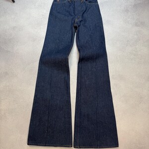 Op de afbeelding: Donkerblauwe denim flared jeans. De jeans heeft een hoge taille en een uitlopende pijp. De voorkant heeft een knoopsluiting en een ritssluiting. De naden zijn zichtbaar en de jeans is in goede staat.