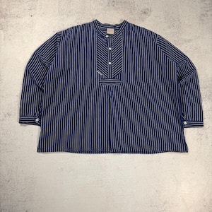 Puede incluir: Una camisa de manga larga a rayas azul marino y blanco con cuello mandarín. La camisa tiene una tapeta abotonada y puños abotonados. Las rayas verticales son blancas sobre un fondo azul marino. La camisa está hecha de una tela ligera.