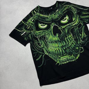 Puede incluir: Camiseta negra con un llamativo dise&ntilde;o de calavera verde ne&oacute;n. La calavera tiene detalles intrincados y est&aacute; rodeada de elementos mec&aacute;nicos verdes. El dise&ntilde;o cubre toda la parte delantera de la camiseta, creando un gr&aacute;fico audaz.