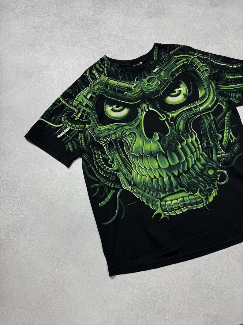 Puede incluir: Camiseta negra con un llamativo dise&ntilde;o de calavera verde ne&oacute;n. La calavera tiene detalles intrincados y est&aacute; rodeada de elementos mec&aacute;nicos verdes. El dise&ntilde;o cubre toda la parte delantera de la camiseta, creando un gr&aacute;fico audaz.