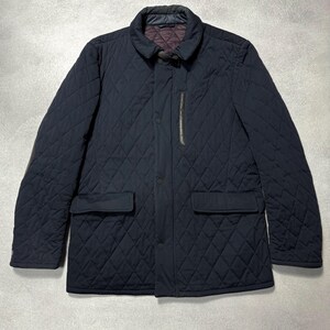 May include: A navy blue quilted jacket with a diamond pattern. The jacket features a collar, two front pockets, and a vertical zipper pocket. It has a button closure and a dark brown interior lining.