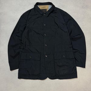 May include: Black jacket with a button-up front, two front pockets, and a collared neckline. The jacket has a quilted design and a light-colored lining visible at the collar. The brand name "Canali" is visible on the collar.