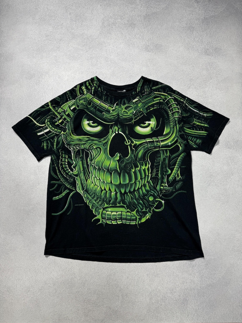 Puede incluir: Camiseta negra con un dise&ntilde;o de calavera verde ne&oacute;n. La calavera tiene ojos brillantes y detalles mec&aacute;nicos. El dise&ntilde;o gr&aacute;fico es detallado y llamativo, cubriendo la parte delantera de la camiseta.