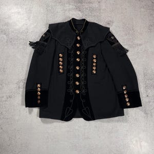 May include: Black jacket with gold buttons and trim. The jacket features a high collar, velvet accents, and decorative gold embroidery. The sleeves have velvet cuffs with gold buttons and small tassels.