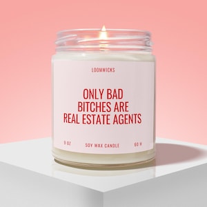May include: A lit soy wax candle in a clear glass jar with a white label. The label features the text LOOMWICKS, 9 OZ, SOY WAX CANDLE, 60 H, and the red text ONLY BAD BITCHES ARE REAL ESTATE AGENTS. The candle has a visible flame at the top.