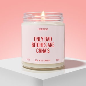 May include: A clear glass jar candle with a white label featuring the red text LOOMWICKS, ONLY BAD BITCHES ARE CRNA'S, 9 OZ, SOY WAX CANDLE, and 60 H. The candle contains white wax and has a lit wick, creating a warm glow from the center of the jar.