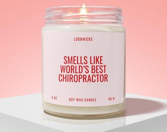 May include: A lit soy wax candle in a clear glass jar with a white label. The label features the text LOOMWICKS, SMELLS LIKE WORLD'S BEST CHIROPRACTOR, 9 OZ, and 60 H in red lettering. The candle has a visible flame and white wax inside the jar.