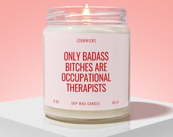 May include: A clear glass jar candle with a white label featuring the red text LOOMWICKS, ONLY BADASS BITCHES ARE OCCUPATIONAL THERAPISTS, 9 OZ, SOY WAX CANDLE, and 60 H. The candle contains white wax and has a lit wick at the top center.