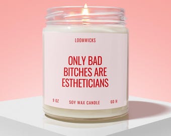 Puede incluir: Una vela de cera de soja en un frasco de vidrio transparente con una etiqueta blanca que presenta el texto rojo LOOMWICKS, ONLY BAD BITCHES ARE ESTHETICIANS, 9 OZ y 60 H. La vela contiene cera blanca y una mecha encendida con llama.
