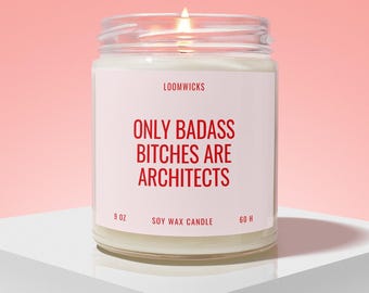 May include: A clear glass jar soy wax candle with a white label featuring the red text LOOMWICKS, ONLY BADASS BITCHES ARE ARCHITECTS, 9 OZ, and 60 H. The candle has a lit wick and is filled with white wax, showing a visible flame at the top.