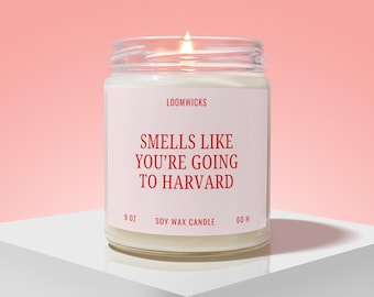 May include: A clear glass jar soy wax candle with a white label featuring the red text LOOMWICKS, SMELLS LIKE YOU'RE GOING TO HARVARD, 9 OZ, and 60 H. The candle has a lit wick and is filled with white wax, presented in a simple cylindrical container.