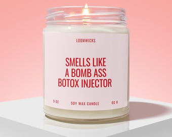 May include: A clear glass jar candle with a white label featuring the red text LOOMWICKS, SMELLS LIKE A BOMB ASS BOTOX INJECTOR, 9 OZ, SOY WAX CANDLE, and 60 H. The candle contains white wax and has a lit wick visible at the top of the jar.