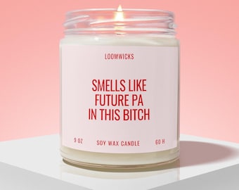 May include: A lit soy wax candle in a clear glass jar with a white label. The label features the text LOOMWICKS, 9 OZ, 60 H, and the phrase SMELLS LIKE FUTURE PA IN THIS BITCH in red lettering. The candle wax is white and the flame is visible.