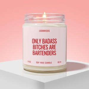 May include: A 9 oz soy wax candle in a clear glass jar with a lit wick. The white label features the text LOOMWICKS, ONLY BADASS BITCHES ARE BARTENDERS, SOY WAX CANDLE, and 60 H in red lettering against a light pink background.
