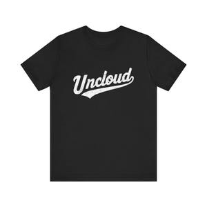 May include: A black short-sleeved t-shirt featuring the word Uncloud printed in a white, distressed, script-style font across the centre of the chest. The garment has a crew neckline and a standard fit with short sleeves and a straight hemline.