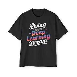 Puede incluir: Una camiseta negra de manga corta con el texto blanco Living that y Dream en fuente cursiva, con la palabra Deep Learning en un degradado multicolor de rosa, naranja y azul, acentuado por pequeños iconos de estrellas de cuatro puntas.