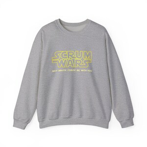 May include: A heather gray sweatshirt with the text "SCRUM WARS" in yellow, styled like the Star Wars logo. Below the text is the phrase "MAY BRUTE FORCE BE WITH YOU". The sweatshirt has a crew neck and long sleeves.