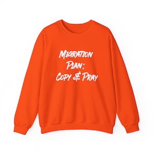 Könnte beinhalten: Ein leuchtend orangefarbenes Sweatshirt mit Rundhalsausschnitt und dem weißen Schriftzug "Migration Plan: Copy & Pray" in einem abgenutzten Pinselstrich-Stil mittig auf der Brust. Das Kleidungsstück hat lange Ärmel und einen gerippten Kragen.