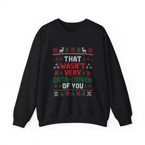 May include: Black crew neck sweatshirt with a festive holiday design. The text "THAT WASN'T VERY DATA-DRIVEN OF YOU" is displayed in a pixelated font, surrounded by reindeer, Christmas trees, and snowflakes in red, green, and white.