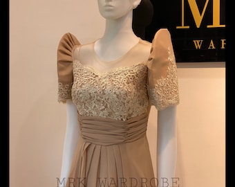 May include: A tan formal dress with a sheer neckline and short, puffed sleeves. The bodice features intricate gold lace detailing, and the skirt is pleated. The dress is displayed on a mannequin. The text "MRK WARDROBE" is visible at the bottom.