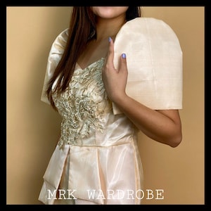 Op de afbeelding: Een cr&egrave;mekleurige Filipiniana-jurk met gouden borduurwerk en een bijpassende cr&egrave;mekleurige sjaal. De jurk heeft een getailleerd bovenstuk en een zwierige rok. De tekst "MRK WARDROBE" is zichtbaar onderaan de afbeelding.