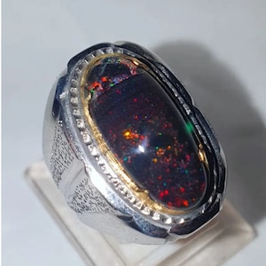 May include: A silver ring with a black opal gemstone set in a gold bezel. The ring has a textured band.
