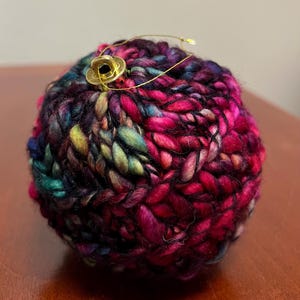 Pu&ograve; includere: Un ornamento lavorato a maglia colorato con un anello e un bottone dorati. L'ornamento &egrave; realizzato in una variet&agrave; di colori, tra cui rosa, viola, blu, verde e nero.