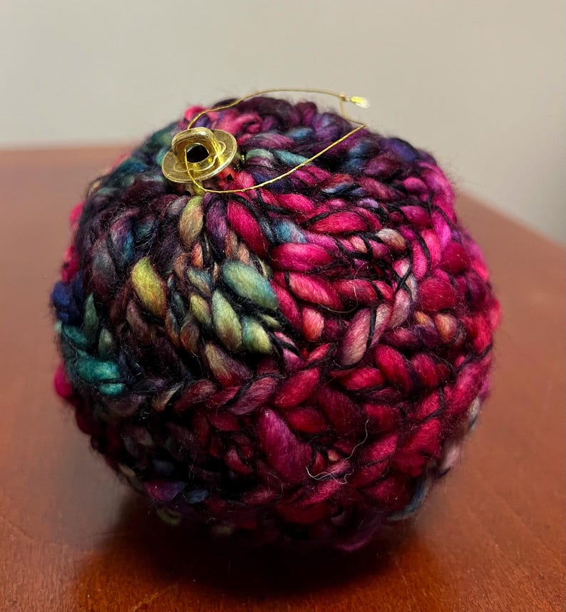 Pu&ograve; includere: Un ornamento lavorato a maglia colorato con un anello e un bottone dorati. L'ornamento &egrave; realizzato in una variet&agrave; di colori, tra cui rosa, viola, blu, verde e nero.