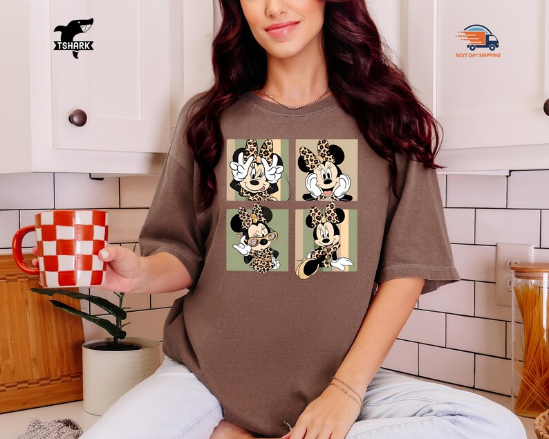 May include: Brown t-shirt featuring a four-panel design of Minnie Mouse in various poses. Each panel showcases Minnie with a leopard print bow and outfit, set against a light green and beige background. The shirt has short sleeves and a relaxed fit.