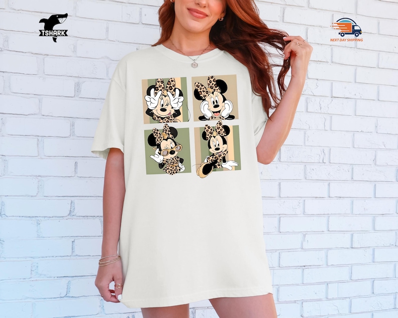 May include: Cream-colored t-shirt featuring a four-panel design of Minnie Mouse in various poses. Each panel showcases Minnie with a leopard print bow and accents. The shirt has a relaxed fit and short sleeves, perfect for casual wear.