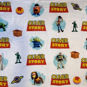 May include: White blanket featuring various characters and logos from the movie "Toy Story". The blanket includes images of Woody, Buzz Lightyear, Rex, and the text "OLIVER STORY" in a red and yellow design. Other characters are also featured.