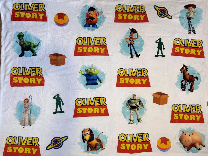 May include: White blanket featuring various characters and logos from the movie "Toy Story". The blanket includes images of Woody, Buzz Lightyear, Rex, and the text "OLIVER STORY" in a red and yellow design. Other characters are also featured.