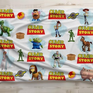 May include: White blanket featuring various characters and the text "OLIVER STORY" in red and yellow. The blanket showcases cartoon figures like a dinosaur, a potato head, a space ranger, and a pig.