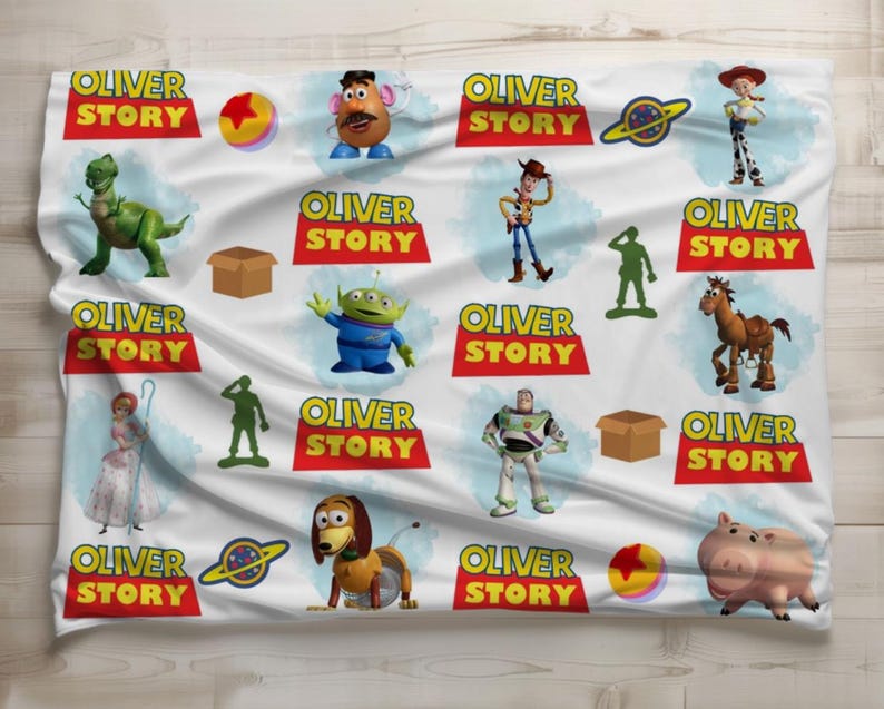 May include: White blanket featuring various characters and the text "OLIVER STORY" in red and yellow. The blanket showcases cartoon figures like a dinosaur, a potato head, a space ranger, and a pig.