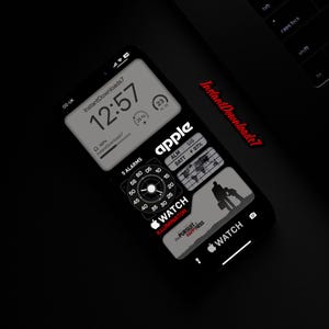 Peut inclure: Un cadran de montre numérique noir et blanc avec le mot "apple" en lettres rouges. Le cadran de la montre comporte une horloge numérique, une boussole et un indicateur de batterie. Le cadran de la montre est entouré d'une lunette noire et d'un bracelet noir.