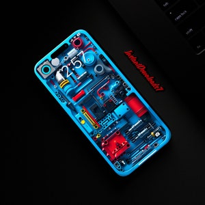 May include: A blue smartphone with a transparent back revealing a complex internal mechanism made of colourful plastic pieces, gears, and wires. The phone's screen displays the time "12:57" and the text "Instant Downloads?" in white.