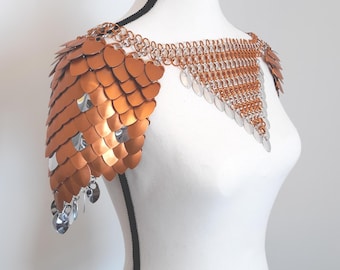 May include: A shoulder mantle constructed from metallic copper-coloured scales and silver-toned chainmail links. The piece features a V-shaped front panel and layered scale sections that drape over the shoulders, secured by interconnected metal rings.