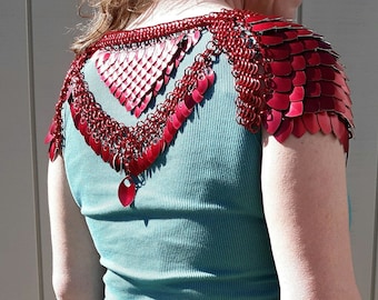 May include: Red chainmail shoulder armour with a scale design. The armour is made of small, interlocking metal scales and rings, creating a layered effect. The armour is worn over a teal ribbed vest top.