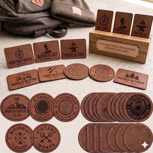Könnte beinhalten: Eine Sammlung brauner Lederaufnäher und Untersetzer mit verschiedenen eingravierten Designs und Texten. Die Aufnäher enthalten Sätze wie "Heritage Goods" und "Wanderlust Trail". Die Untersetzer zeigen Bilder und Sätze wie "Born to be Wild."